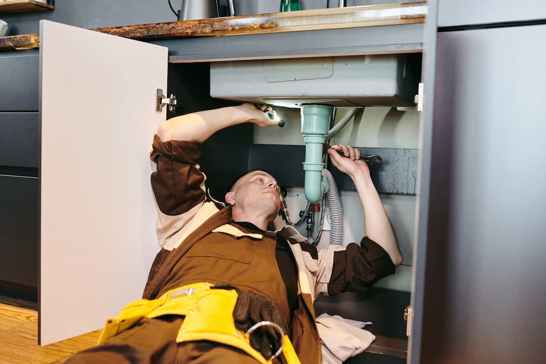 Plumber lying on his back fixing pipes behind an access panel